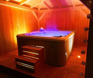 A wooden sauna with a hot tub, a wooden bench, and a ceiling with wooden beams.