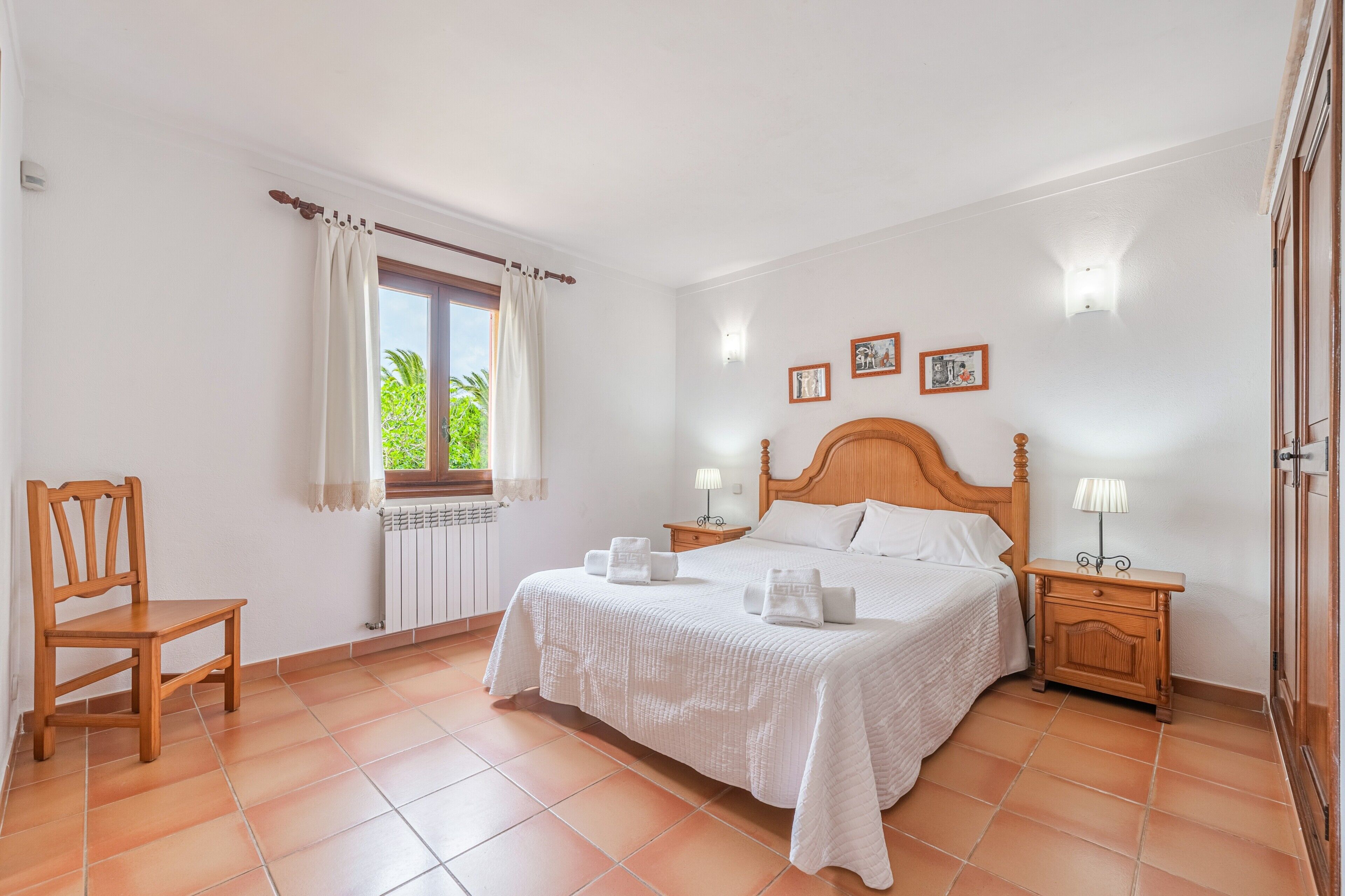 A bedroom with a wooden bed, a chair, a nightstand, and a window with curtains.