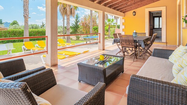 An outdoor patio with wicker furniture, a glass-top table, and yellow chairs. - Peaceful location with pool - Villa Can Jaume (Pollença)
