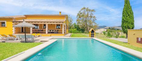 A swimming pool with lounge chairs, a covered seating area, and a building with a yellow facade.