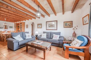 A living room with a wooden ceiling, a sofa set, a coffee table, and a dining area with chairs and a table.