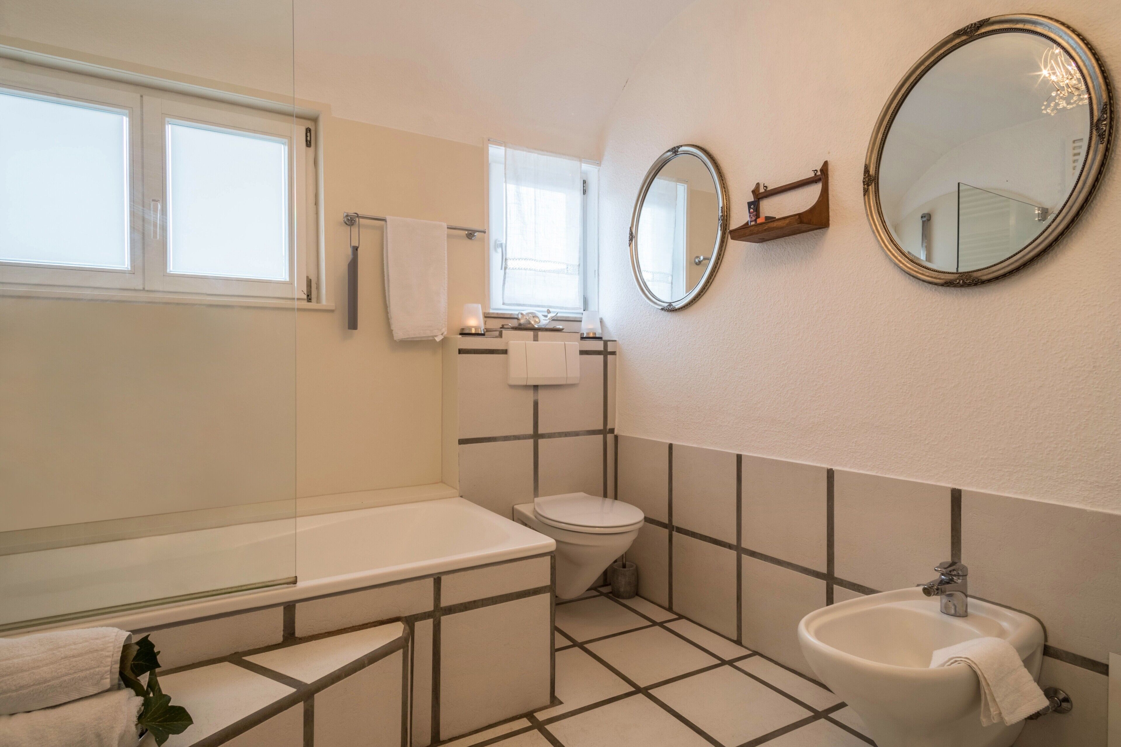 A bathroom with a bathtub, toilet, sink, and two mirrors.