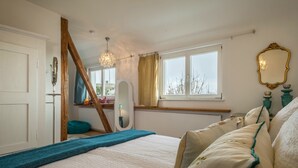 Um quarto com cama, janela, espelho e lustre.