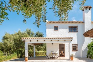 Un bâtiment blanc avec un toit en tuiles, un patio couvert avec une table et des chaises, et une plante en pot.