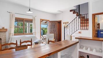 A dining area with a wooden table, chairs, a hanging light fixture, and a view of the outdoors through a window.