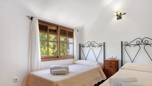 Una camera da letto con due letti, una finestra con tende, un comodino e una lampada a parete.