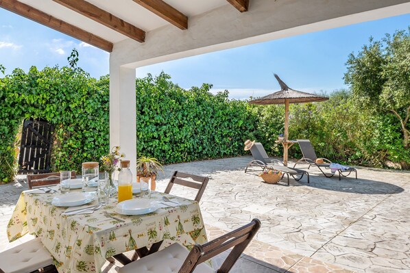 An outdoor patio with a table set for dining, lounge chairs, and a pergola with a roof.