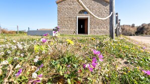 En stengårdskirke med en rebstang, omgivet af vilde blomster.