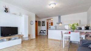 En moderne stue med et fladskærms-tv, en sofa og et spiseområde med stole og et bord.