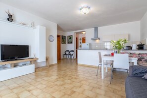 A modern living room with a flat-screen TV, a sofa, and a dining area with chairs and a table.