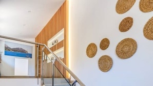 Una moderna scala con ringhiere in vetro e dettagli in legno, che porta a un pianerottolo con un quadro incorniciato.