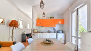 A modern kitchen with white cabinets and a dining area with a wooden table. - Modern apartment with garden, air conditioning and Wi-Fi (LACONA - CAPOLIVERI (LIVORNO))