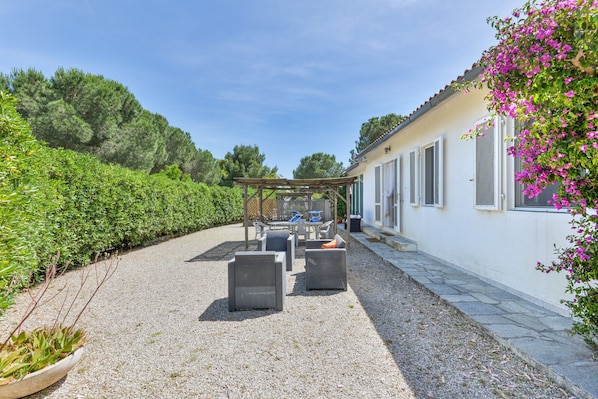 Un patio con mobiliario exterior, una pérgola y un edificio con ventanas.