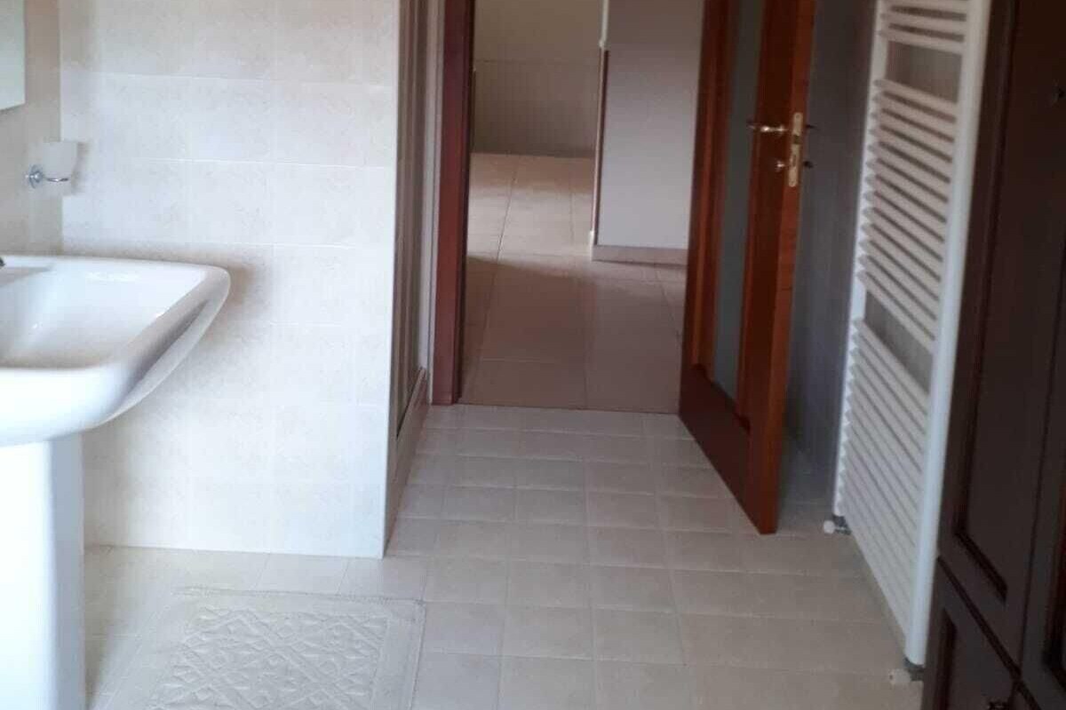A narrow hallway with a sink on the left, a door at the end, and a radiator on the right.