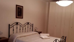 A single bed with a metal frame, a bedside table, a hanging light fixture, and a door in a room with plain walls and tiled flooring. - B&B Porta del Gargano (San Marco in Lamis)