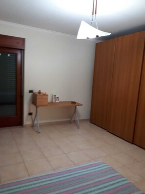 Quarto com armário de madeira, escrivaninha com luminária e tapete listrado no chão.