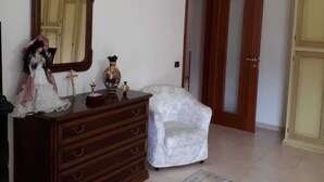 A room with a wooden dresser, a white armchair, a mirror, and a door. - B&B Porta del Gargano (San Marco in Lamis)