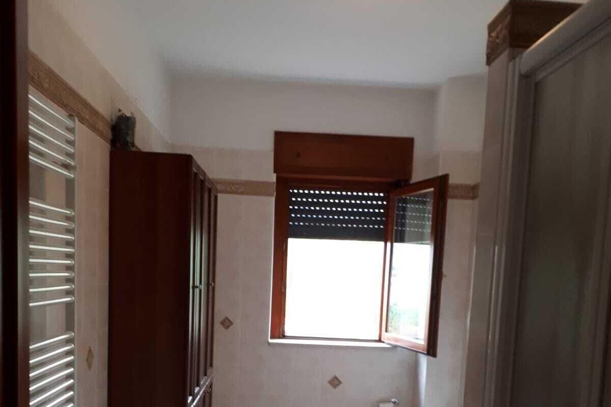 Een smalle gang die uitkomt bij een badkamer met toilet en een raam.