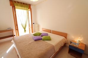 A bedroom with a bed, pillows, a nightstand, a radiator, and a window with curtains.