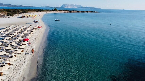 Une plage avec des parasols et des chaises longues, un bateau et une montagne en arrière-plan.