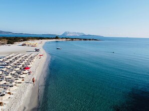 Une plage avec des parasols et des chaises longues, un bateau et une montagne en arrière-plan.