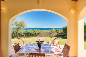 An outdoor patio with a table set for dining, a bottle of champagne, and a view of the sea. - Dreamlike apartment with sea view - Villa Ambra (San Teodoro)