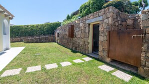 Un bâtiment en pierre avec une porte, un chemin pavé et une haie en arrière-plan.