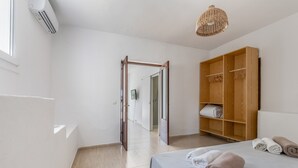 Una camera d'albergo con un letto, un armadio, una lampada a sospensione e una porta che dà su un'altra stanza.