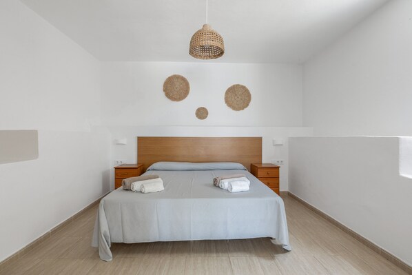 Un dormitorio minimalista con cabecera de madera, cama con ropa de cama azul claro, dos mesitas de noche y una lámpara de fibra.