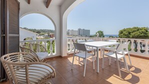 Una terrazza con sedie e tavolo bianchi, vista sul mare e un edificio sullo sfondo.