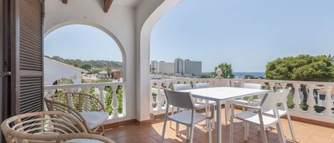 A terrace with white chairs and a table, a view of the sea, and a building in the background.