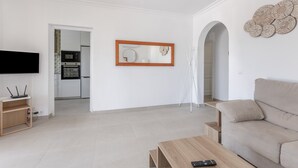 Un soggiorno moderno con un divano, un tavolino, una televisione e una cucina sullo sfondo.
