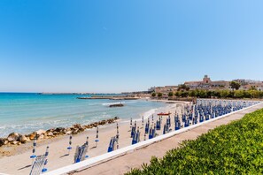 A coastal view with a beach, umbrellas, and a building in the background. - Beach Holidays in Otranto – Casa Federica (Otranto)