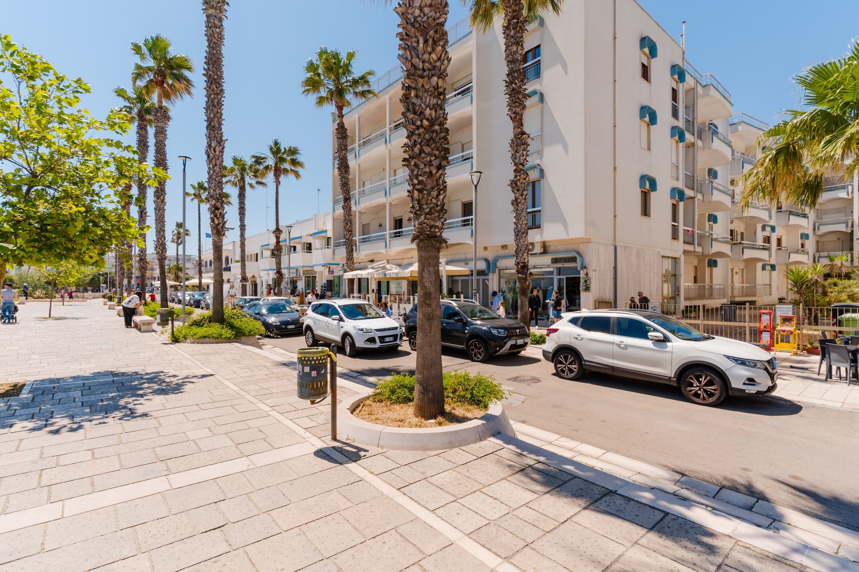 A hotel with multiple floors, palm trees, and parked cars on the street.