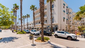 Un hotel de varios pisos, con palmeras y coches estacionados en la calle.