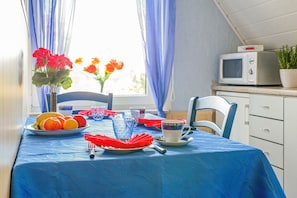 Una mesa de comedor con mantel azul, un plato de fruta, un florero con flores y un microondas en la encimera.