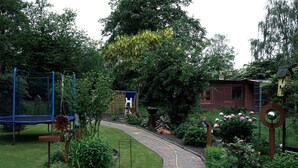 Een tuin met een gebogen pad van bakstenen, een trampoline en een houten constructie.
