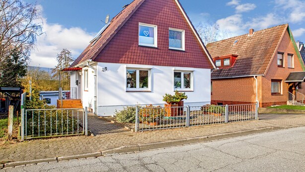 Een woonhuis met twee verdiepingen, een rood dak, witte muren en een kleine voortuin.