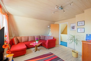 Una sala de estar moderna con un sofá modular, una mesita con un florero, una planta en maceta y un escritorio con una computadora.