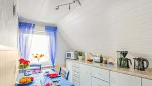 Een keuken met een eettafel voor twee personen, een magnetron, een koffiezetapparaat en een raam met gordijnen.