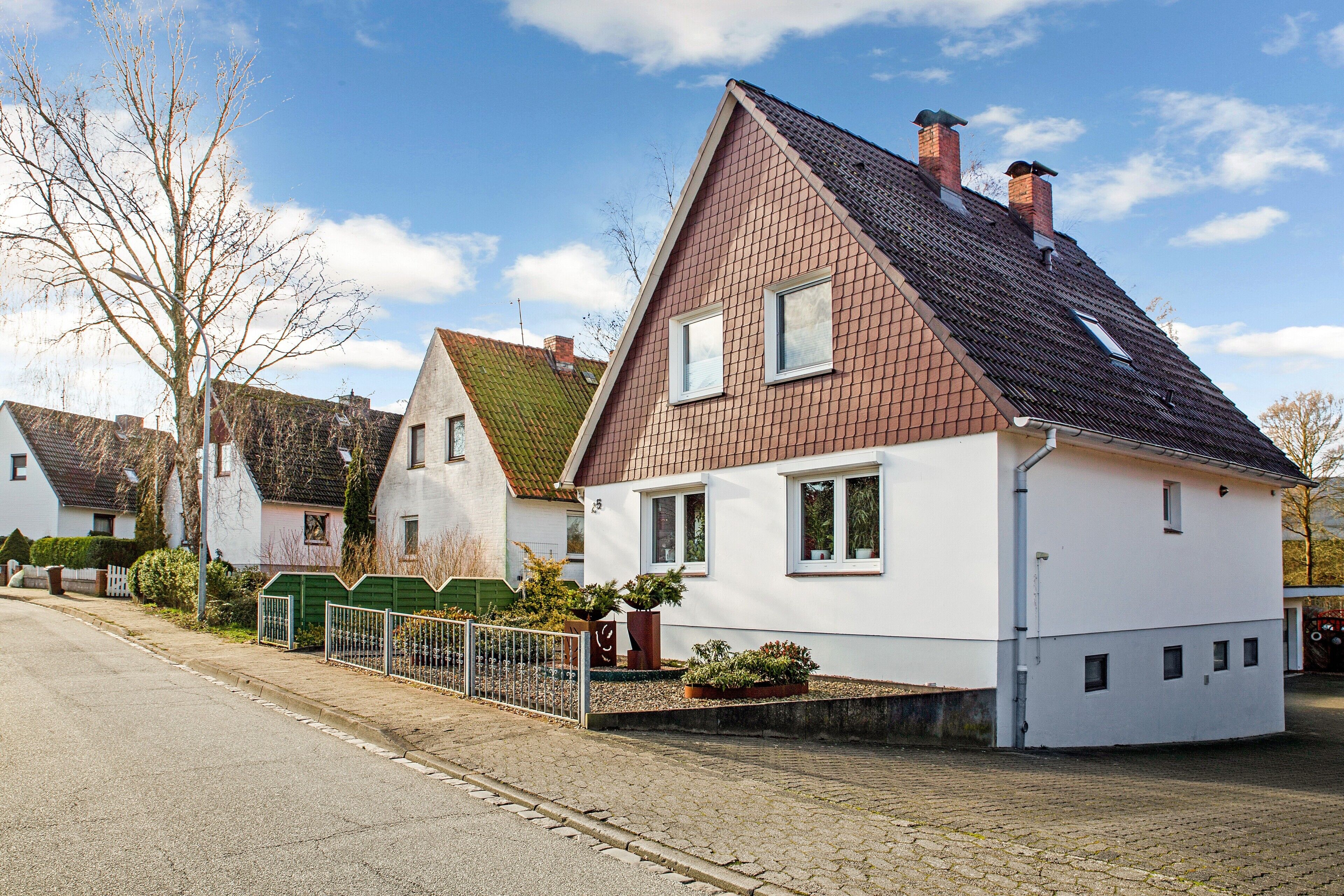 A residential house with a sloped roof, a fenced yard, and a paved driveway.