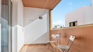 A balcony with a white chair, a small table with a potted plant, and a hanging basket.
