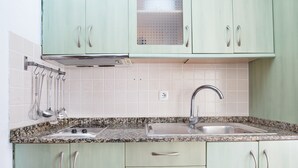 A kitchen with light green cabinets, a granite countertop, a double sink, and stainless steel utensils hanging on the wall.