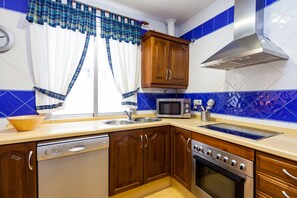 A kitchen with wooden cabinets, a dishwasher, a microwave, a stove, and a window with curtains.