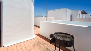 A rooftop terrace with a grill, white walls, and a clear blue sky.