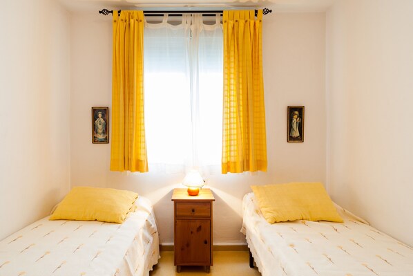 A bedroom with two beds, a nightstand with a lamp, and two wall-mounted pictures.