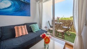 A room with a dark blue sofa, a painting of a wave, a vase with flowers, and a view of an outdoor patio with a table and chairs. - Modern and only a few steps from the sea - Apartamento Soñac S (Los caños de meca ( Cadiz))