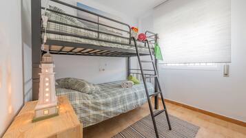 A bunk bed with a ladder, a small table with a decorative item, and a window with blinds.