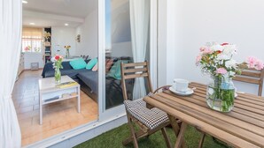 A modern living room with a sofa, a dining table, and a glass door leading to a balcony. - Modern and only a few steps from the sea - Apartamento Soñac S (Los caños de meca ( Cadiz))