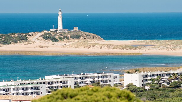A coastal view with a lighthouse, sandy beach, and a row of white buildings. - Modern and only a few steps from the sea - Apartamento Soñac S (Los caños de meca ( Cadiz))